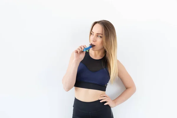Atraktivní sportovní fitness žena držící proteinovou tyčinku na bílém pozadí — Stock fotografie