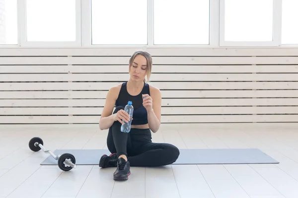 Concepto de personas, deporte y fitness: mujer joven bebiendo agua de la botella deportiva mientras está sentada en la esterilla — Foto de Stock