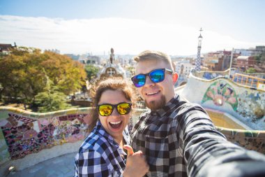 Komik genç çift kamera ile akıllı telefon Park Guell, Barselona, İspanya, gülümseyen fotoğrafı çekmek.