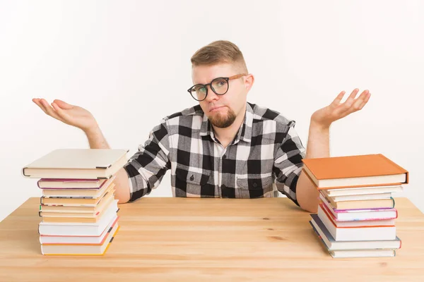 Examen, conocimiento y concepto de educación - confundido estudiante sentado a la mesa con montañas de libros — Foto de Stock