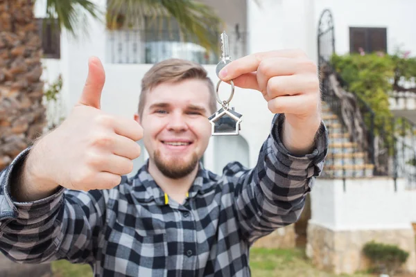 Property, ownership, new home and people concept - young man with keys standing outside new home — Stock Photo, Image