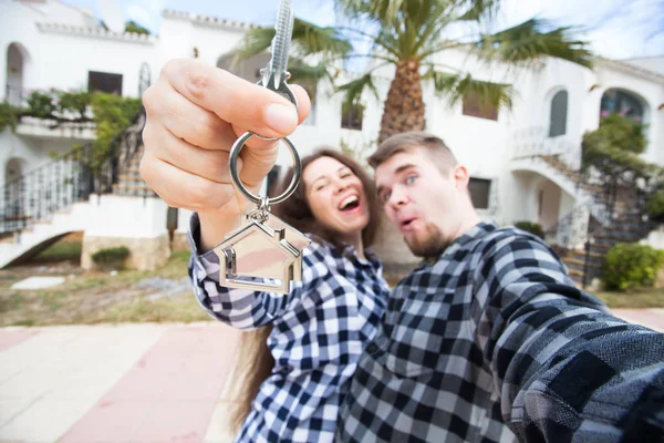 Propiedad, bienes raíces y concepto de alquiler - Feliz joven pareja sonriente mostrando las llaves de su nueva casa —  Fotos de Stock