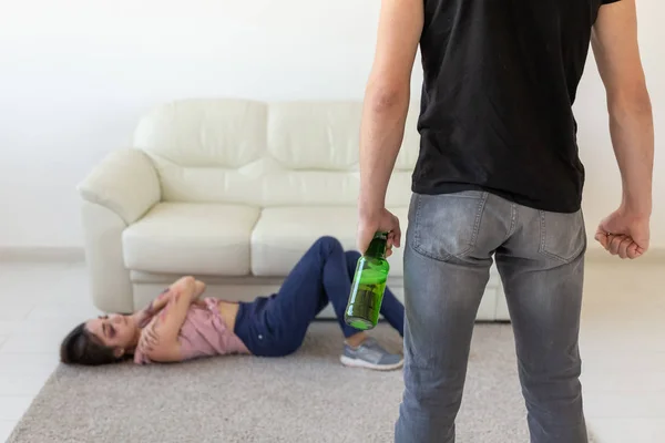 Vítima, violência doméstica, abuso e conceito alcoólico - homem bêbado com garrafa perto de sua esposa deitada no chão — Fotografia de Stock