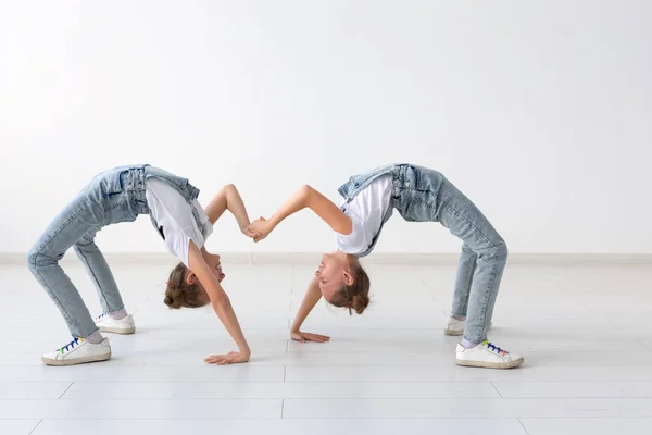 Conceito de família e esporte - Duas meninas gêmeas acrobata estão de pé nas mãos sobre fundo branco — Fotografia de Stock