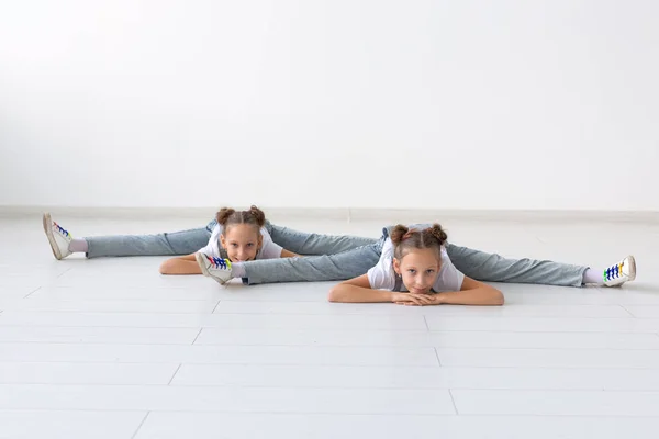 Pessoas, crianças e conceito acrobático - pequenas irmãs gêmeas fazendo exercícios em fundo branco — Fotografia de Stock