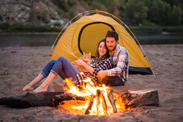 Menschen, Tourismus und Naturkonzept - Mann und Frau mit Katze sitzen am Feuer — Stockfoto