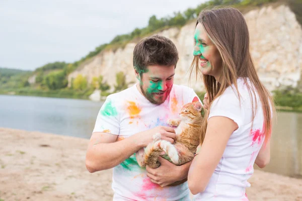 Фестиваль холи, праздники, туризм, питомцы и природа - Портрет женщины и мужчины с кошкой, покрытой разноцветной пылью — стоковое фото