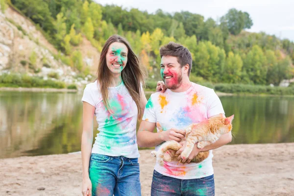 Festival Holi, Urlaub, Tourismus, Haustier und Naturkonzept - Portrait von Frau und Mann mit Katze bedeckt mehrfarbigem Staub — Stockfoto