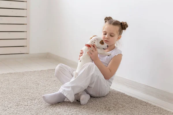 People, pets and animal concept - Little girl sitting on the floor over white background and holding puppy Jack Russell Terrier