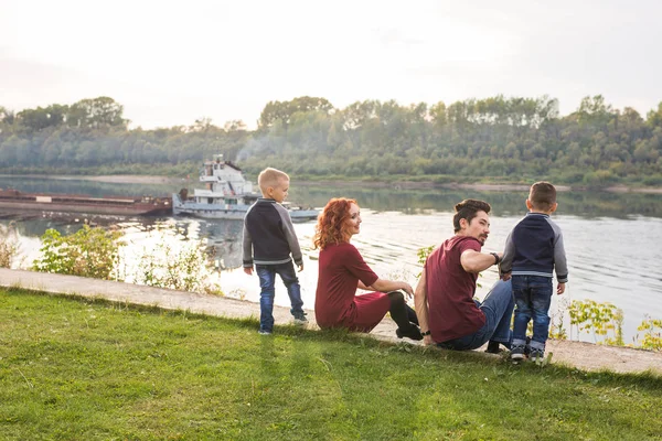 Elternschaft, Kindheit und Naturkonzept - Familie sitzt auf dem grünen Boden und blickt auf ein kleines Boot — Stockfoto