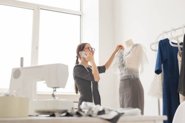 Terzi, terzi, moda ve showroom konsept - güzel genç tasarımcı cep telefonda konuşurken ve terzilik stüdyo işinde incelenirken gülümseyen