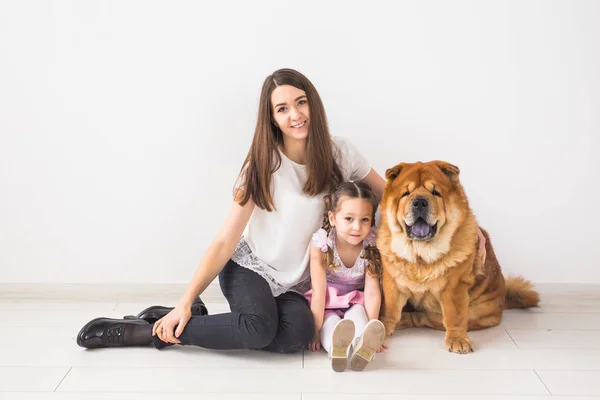 Mascotas, niños y concepto familiar - Niña y su madre abrazando perro chow-chow sobre fondo blanco — Foto de Stock