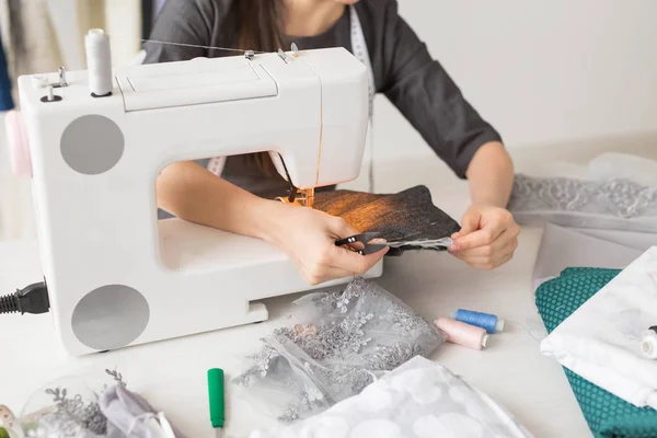Concepto de personas, moda y sala de exposición - joven diseñador de moda cose la ropa en una máquina de coser de cerca — Foto de Stock