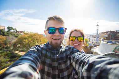 Komik genç çift kamera ile akıllı telefon Park Guell, Barselona, İspanya, gülümseyen fotoğrafı çekmek.