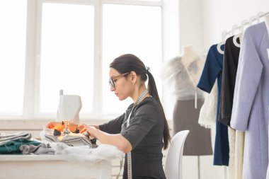 İnsanlar, terzi ve moda kavramı - yan görünüm portre moda tasarımcısı bardaklarda atölyede dikiş makinesi kullanma