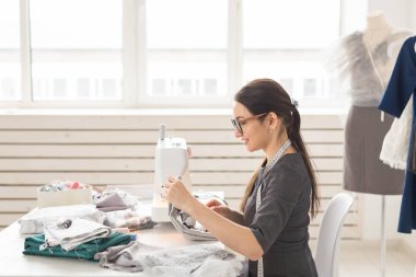 İnsanlar ve moda kavramı - genç terzi kadın dikiş makinesi giysilerini diker.