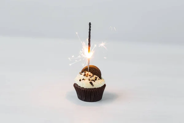 Voedsel, vakantie, happy birthday, bakkerij en desserts concept - heerlijke cupcake met sparkler op witte tafel. — Stockfoto