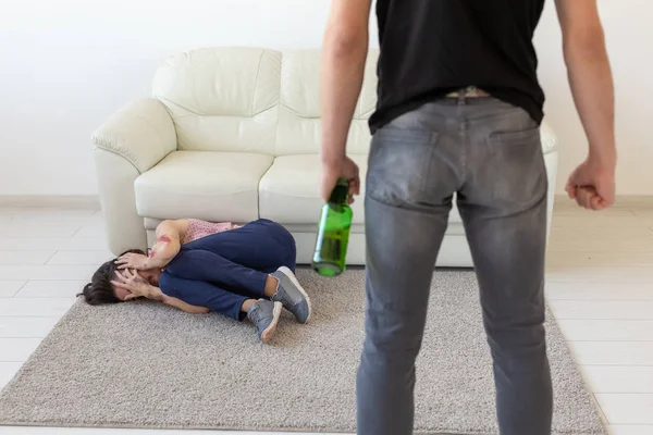 Víctima, violencia doméstica, abuso y concepto alcohólico - hombre borracho con botella cerca de su esposa tirada en el suelo —  Fotos de Stock