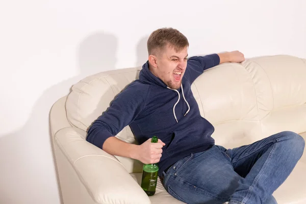 Concepto de depresión y alcoholismo: joven agresivo sentado en un sofá con una botella de alcohol —  Fotos de Stock