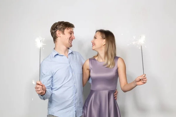 Conceito de festa, família e feriados - jovem casal segurando sparklers no fundo branco — Fotografia de Stock