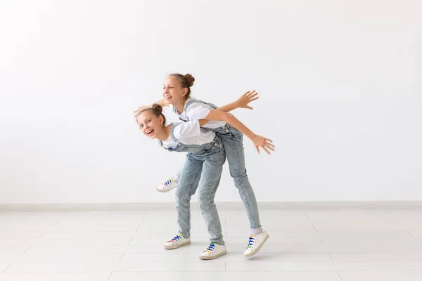 Personas, niños y concepto familiar - niña llevando a su hermana gemela a cuestas sobre fondo blanco — Foto de Stock