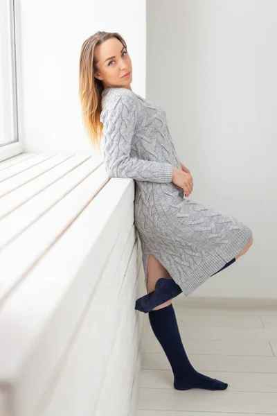 Pessoas, moda e conceito de beleza - jovem mulher em vestido de lã posando perto peitoril da janela — Fotografia de Stock
