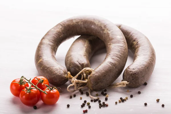 Food, meat and delicious concept - Close up of horse meat sausage with cumin and pepper over white background — Stock Photo, Image