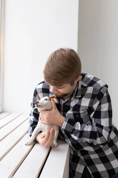 People, pets and animals concept - young man hugging puppy near window on white background — Stock Photo, Image