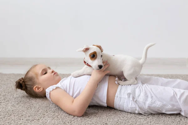 Crianças, animais de estimação e animais conceito - Pequena menina adorável engraçado deitado no chão com filhote de cachorro — Fotografia de Stock