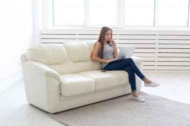 Teknolojileri, serbest ve insanlar kavramı - beyaz kanepede oturan ve içinde belgili tanımlık laptop chat yapan genç kadın