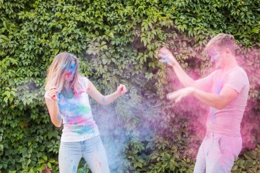 Tatil, bayram ve insanlar kavramı - mutlu çift yüzlerinde çok renkli toz ile eğleniyor