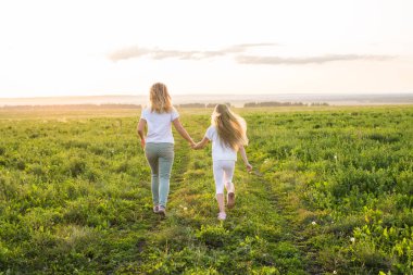 Aile, yaz ve tatil kavramı - Back view bir ışığa doğru çalışan kızı elini tutan anne