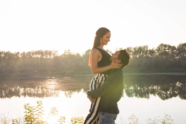 Romantique, amour, concept de personnes - jeune couple étreignant près du lac au coucher du soleil — Photo