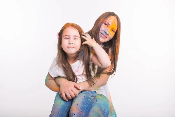 Familia, festival de holi y el concepto de la gente - mujer e hija pequeña divirtiéndose con polvo de colores sobre fondo blanco — Foto de Stock