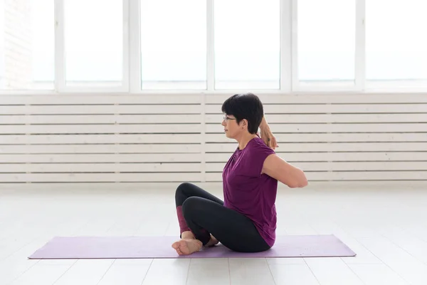 Personas, yoga, deporte y concepto de salud - mujer atractiva estirando las manos sentado en la esterilla de yoga en el fondo de la habitación blanca —  Fotos de Stock