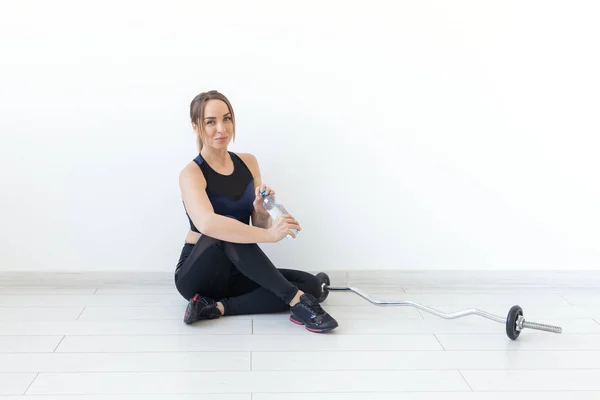 Gente, deporte y fitness concepto - mujer joven sentada con botella de agua en la alfombra del gimnasio. Fondo con espacio de copia — Foto de Stock