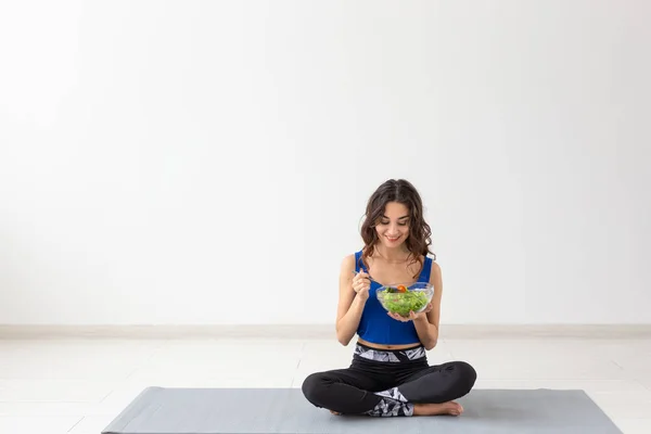 Estilo de vida saludable, personas y concepto deportivo - Mujer de yoga con un tazón de ensalada de verduras después de entrenar sobre fondo blanco —  Fotos de Stock