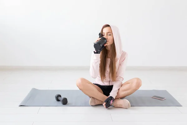Estilo de vida saludable, personas y concepto de deporte - Mujer sonriente sentada en la esterilla de yoga y agua potable después del entrenamiento duro —  Fotos de Stock