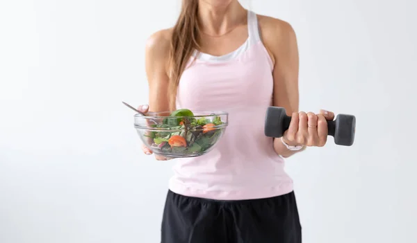 Egészséges életmód, az emberek koncepció - egy tányér saláta az egyik kezében, és a súlyzó, a másik kezében. Mosoly és fitness ruha — Stock Fotó