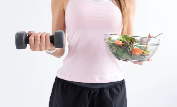 Ernährungs-, Ernährungs- und Fitnesskonzept - Nahaufnahme von gesundem Salat und Hantel in weiblicher Hand vor weißem Hintergrund — Stockfoto