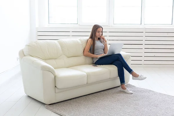 Technologies, freelance et concept de personnes - jeune femme assise sur le canapé blanc et bavardant dans l'ordinateur portable — Photo