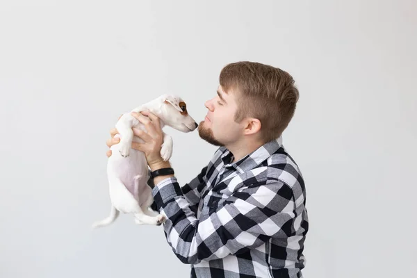 Concepto de personas, mascotas y animales - hombre joven besando gato russell terrier cachorro sobre fondo blanco — Foto de Stock