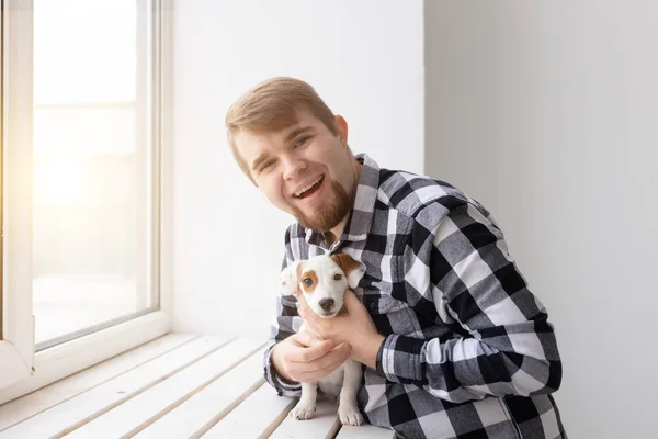 Gente y concepto de mascota - Hombre feliz sosteniendo un perro Jack Russell Terrier sobre el fondo de la ventana — Foto de Stock
