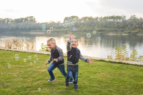 Children and childhood concept - Two brothers boys playing with colorful soap bubbles — Stock Photo, Image