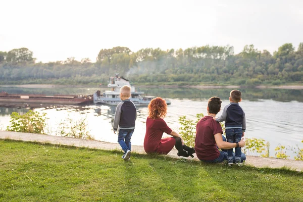 Elternschaft, Kindheit und Naturkonzept - Familie sitzt auf dem grünen Boden und blickt auf ein kleines Boot — Stockfoto