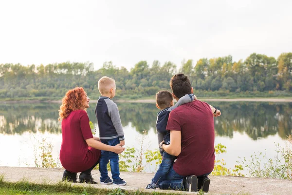 Föräldraskap, barndom och familj koncept - föräldrar och två manliga barn promenader i parken och titta på något, bakifrån — Stockfoto