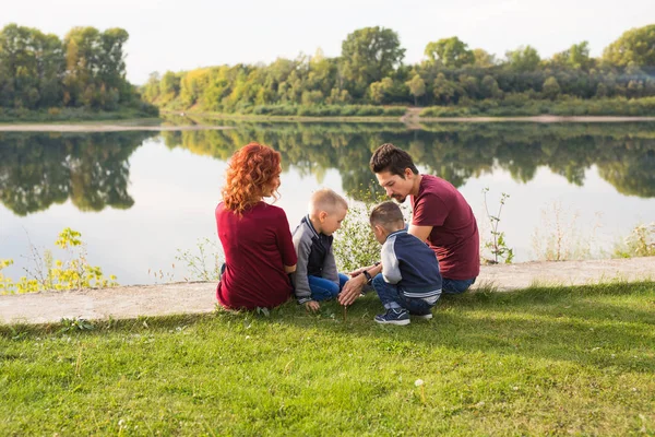 Föräldraskap, natur, människor koncept - familj med två söner sitter nära sjön — Stockfoto