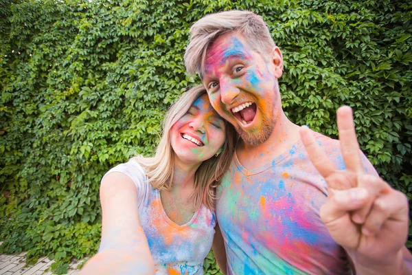 Holiday, holi and people concept - Woman and man with painted faces taking selfie over bush backgrund — Stock Photo, Image