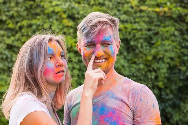 Conceito de férias, holi e pessoas - Casal feliz se divertindo com pó multicolorido em seus rostos — Fotografia de Stock