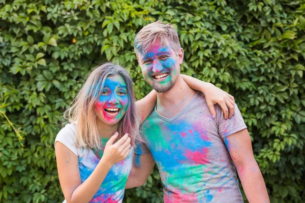 Conceito de férias, holi e pessoas - Mulher sorridente e homem posando com pó multicolorido em seus rostos — Fotografia de Stock